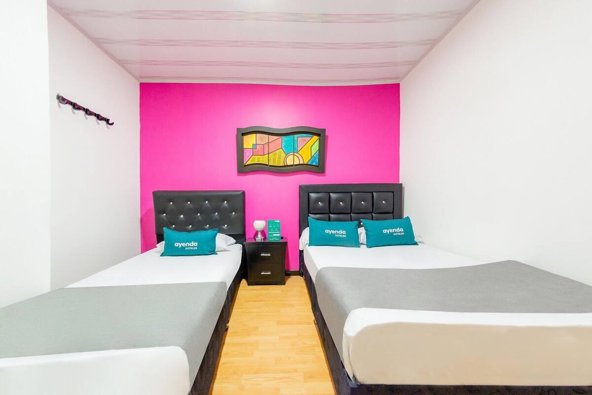 Een hotelkamer met twee bedden, een houten vloer, een roze muur en een lijst met een foto.