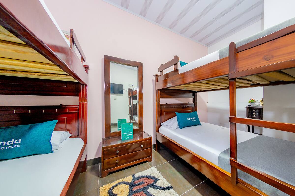 Een hotelkamer met twee stapelbedden, een houten dressoir, een spiegel en een klein tafeltje met een plant.
