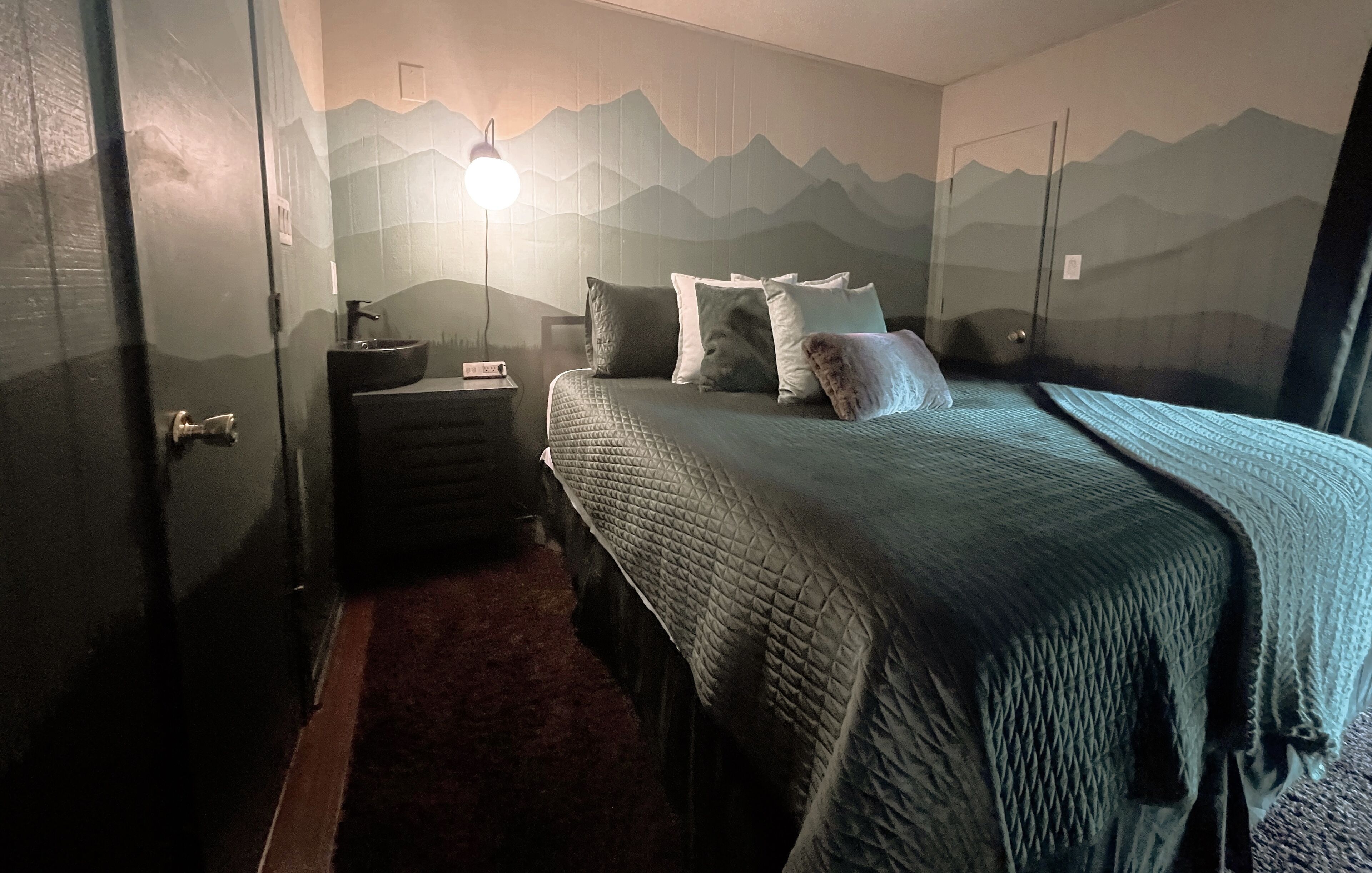 Een slaapkamer met een bed, nachtkastje, lamp en behang met een muurdecoratie.