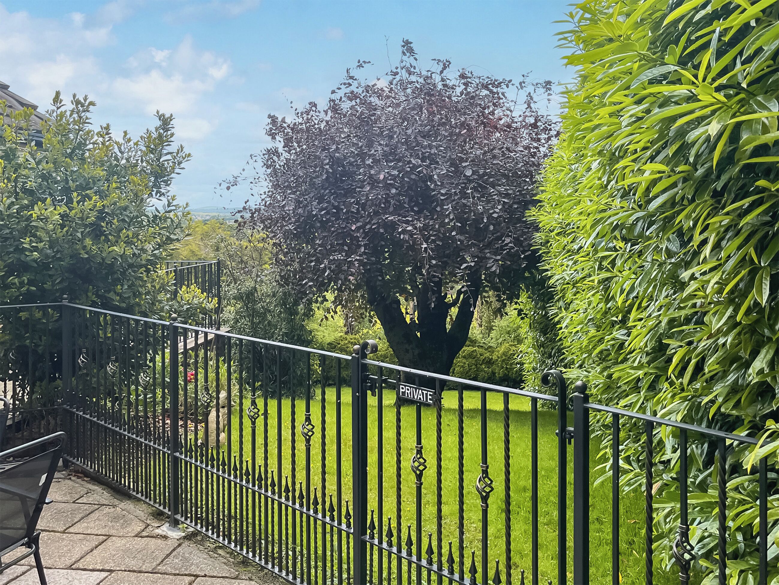 A private garden with a metal fence, a large tree, and well-maintained grass.