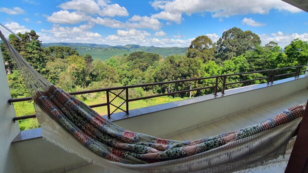A hammock on a balcony with a view of a lush landscape. - Condominio Aspen (Nova Petropolis)