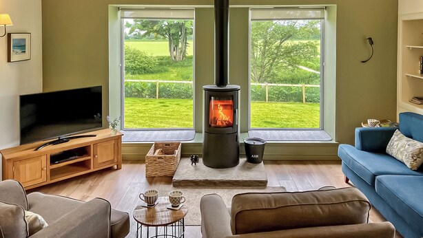 Una sala de estar con chimenea, televisión y vistas a un paisaje verde a través de amplios ventanales.