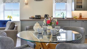 Una cocina moderna con una mesa de comedor de vidrio, sillas tapizadas en gris y un florero con flores.