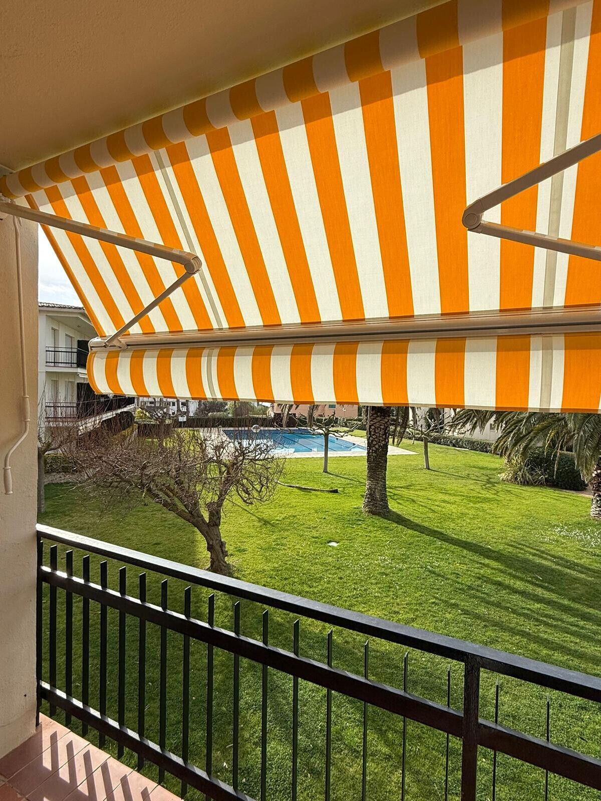 A balcony with a striped awning, a pool, and a well-maintained lawn.