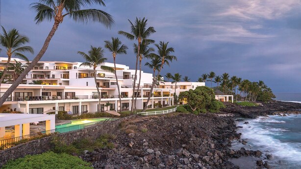 Un hotel frente al mar con varios balcones, piscina y costa rocosa.