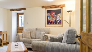 Uma sala de estar com sofá listrado, mesa de centro de madeira e um quadro de cavalos na parede.