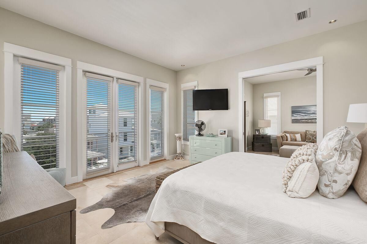 A bedroom with a large bed, a dresser, a TV mounted on the wall, and a view through the sliding glass doors.