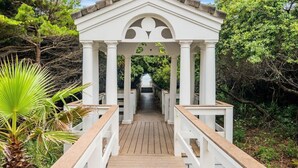 Un gazebo bianco con veranda in legno e ringhiere bianche, immerso nel verde.