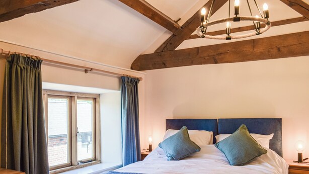 Een slaapkamer met een groot bed, houten balken, een raam met gordijnen en een kroonluchter.