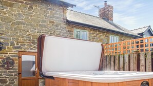 Een houten jacuzzi met deur, voor een stenen muur met houten omheining en houten terras.