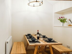 Ein Essbereich mit einem Holztisch, gedeckten Plätzen für vier Personen, schwarzen Tellern und einer Weinflasche.