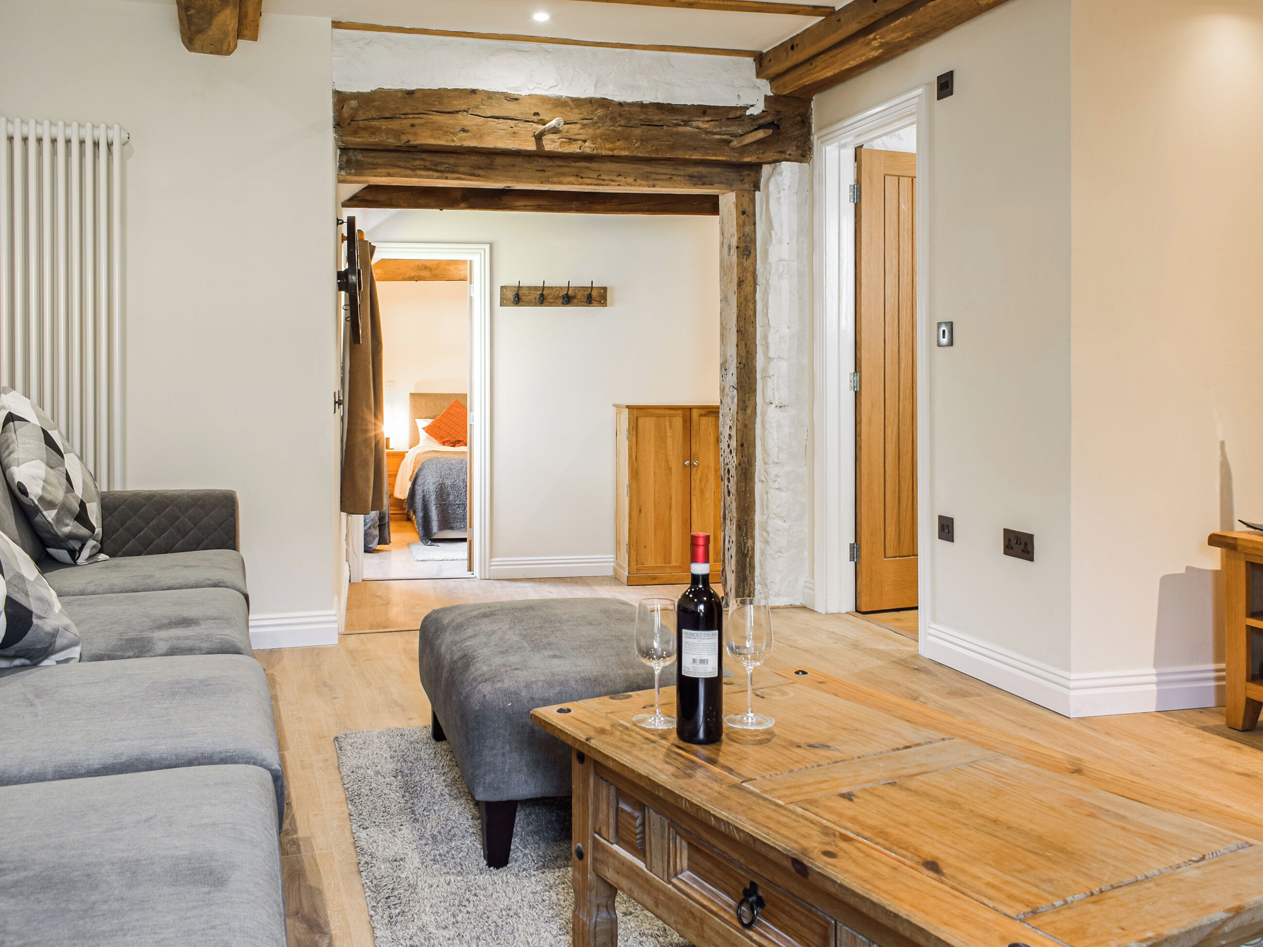 Un salon chaleureux avec une table basse en bois, un canapé gris et un pouf assorti. Une bouteille de vin et des verres sont posés sur la table.