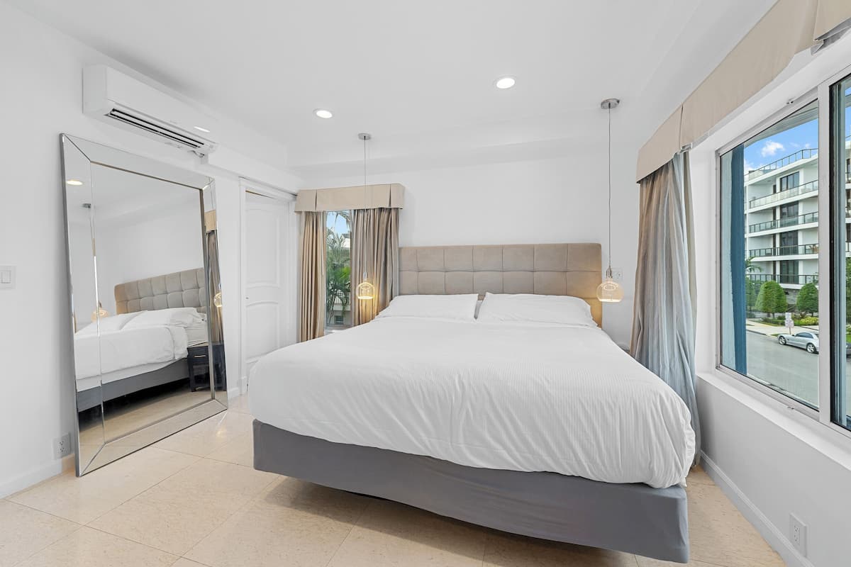Quarto moderno com uma cama grande, um espelho e vista para o exterior.