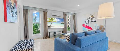Un salon moderne avec un canapé bleu, un banc à motifs zébrés et une grande fenêtre donnant sur une plage.
