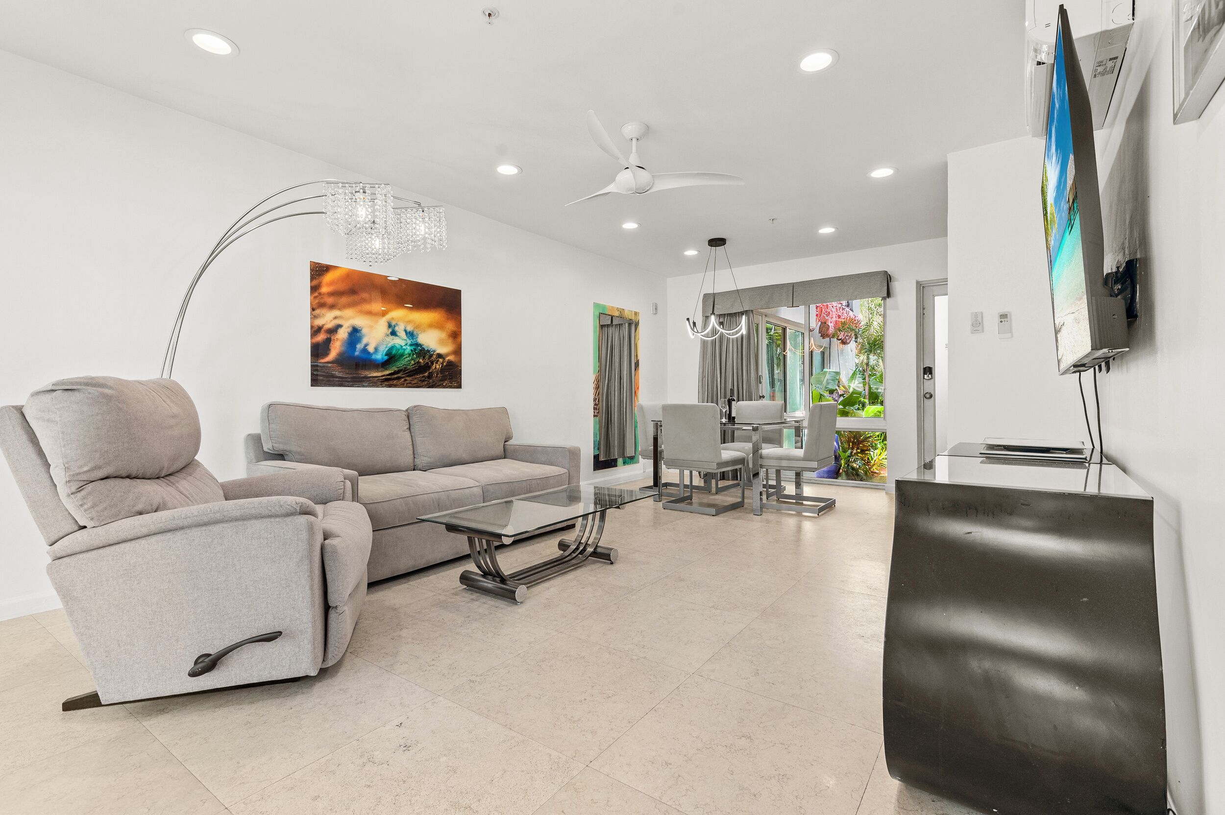 A modern living room with a sofa, a glass coffee table, a chandelier, and a painting on the wall.