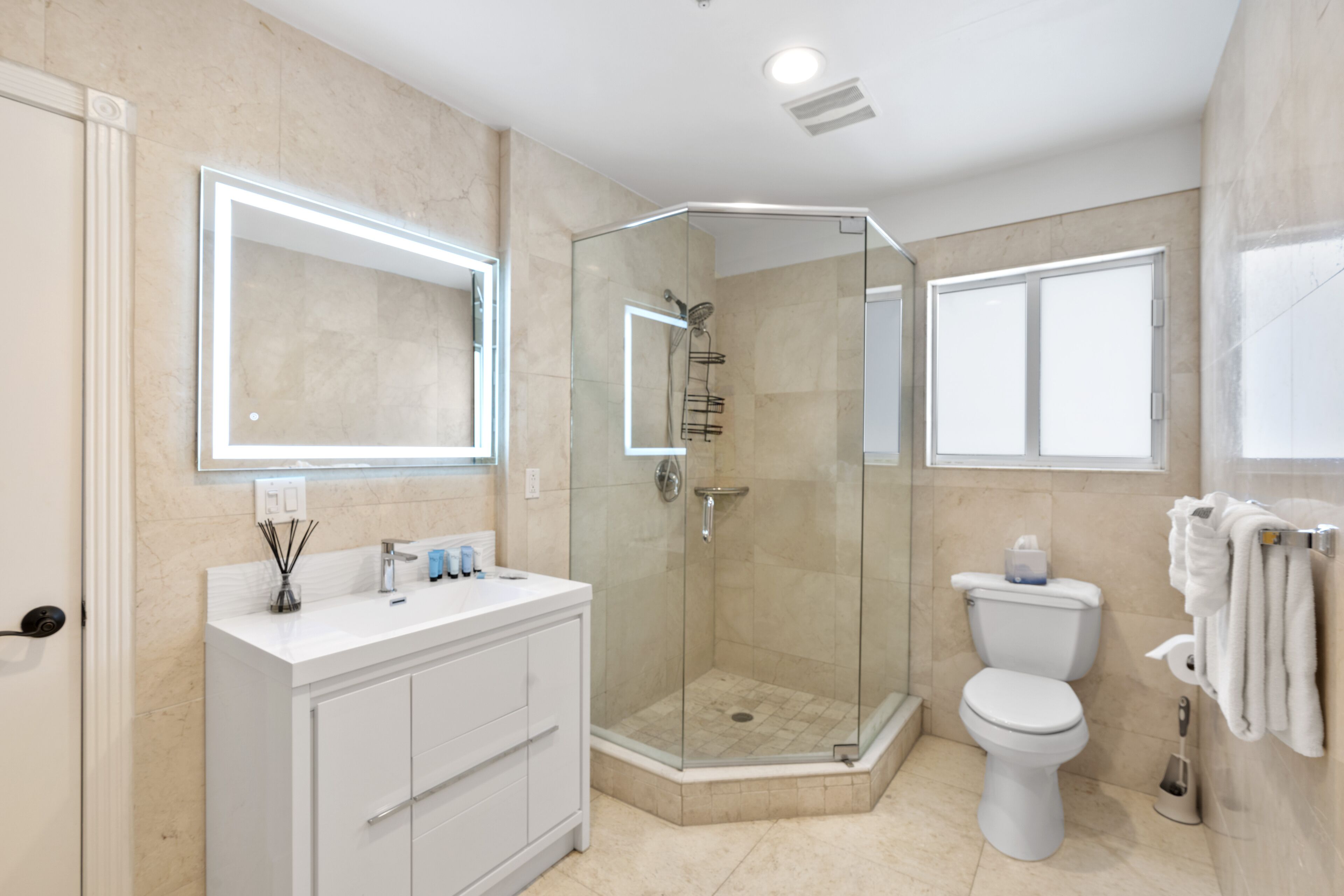 A modern bathroom with a glass-enclosed shower, a white vanity with a mirror, and a toilet with a towel rack.