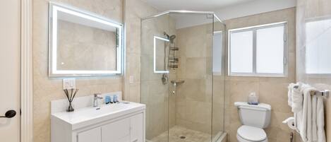 A modern bathroom with a glass-enclosed shower, a white vanity with a mirror, and a toilet with a towel rack.