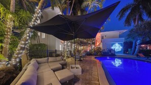 A poolside area with a lounge chair, umbrella, and a pool with a blue light. - Isle of Venice (Fort Lauderdale)