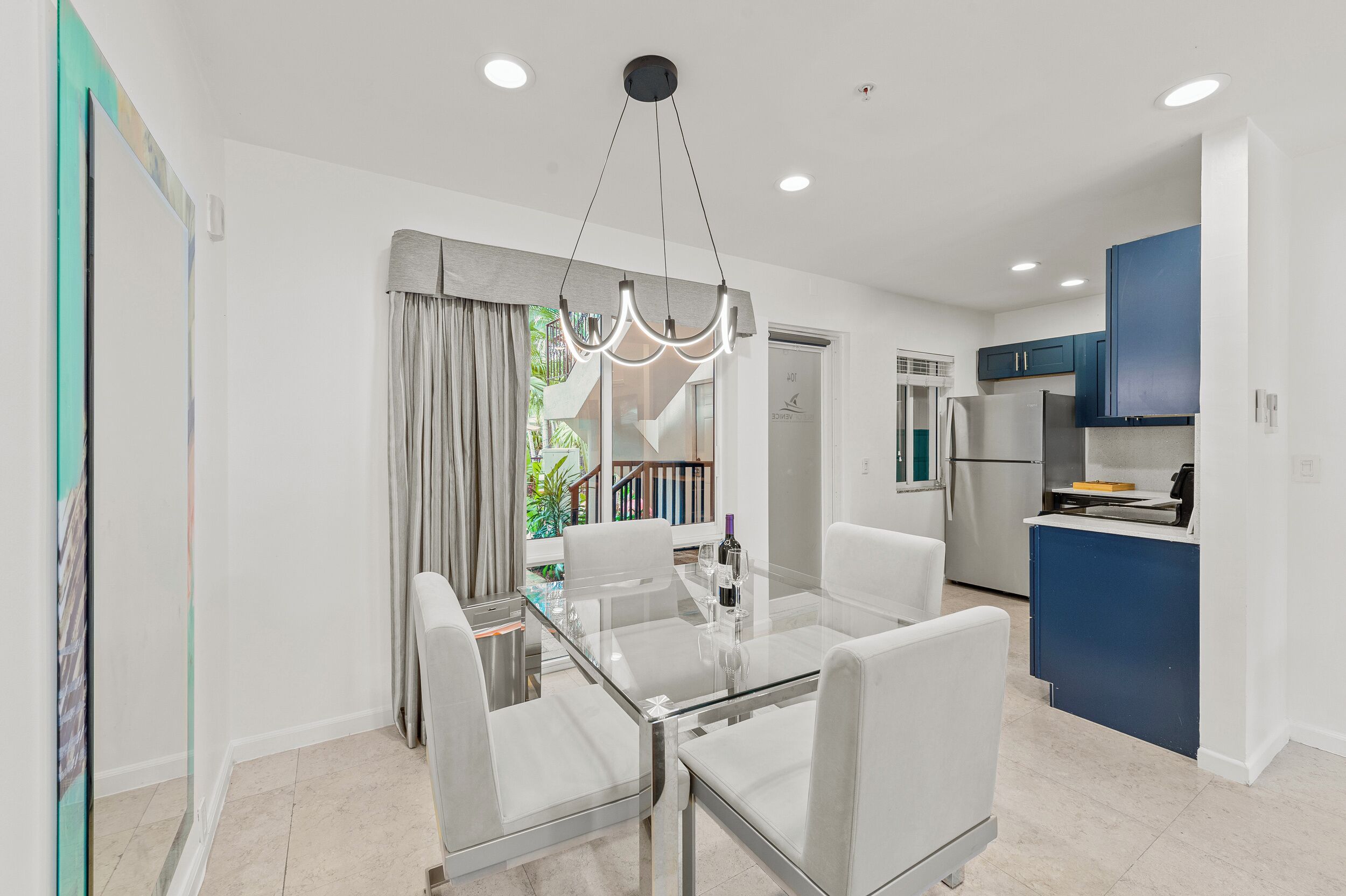 A modern kitchen with blue cabinets, a glass dining table, and a chandelier.