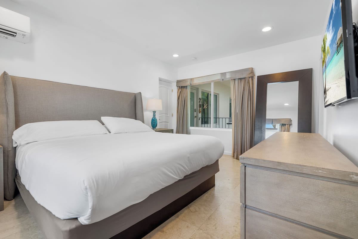 Quarto de hotel moderno com uma cama grande, penteadeira e televisão na parede.