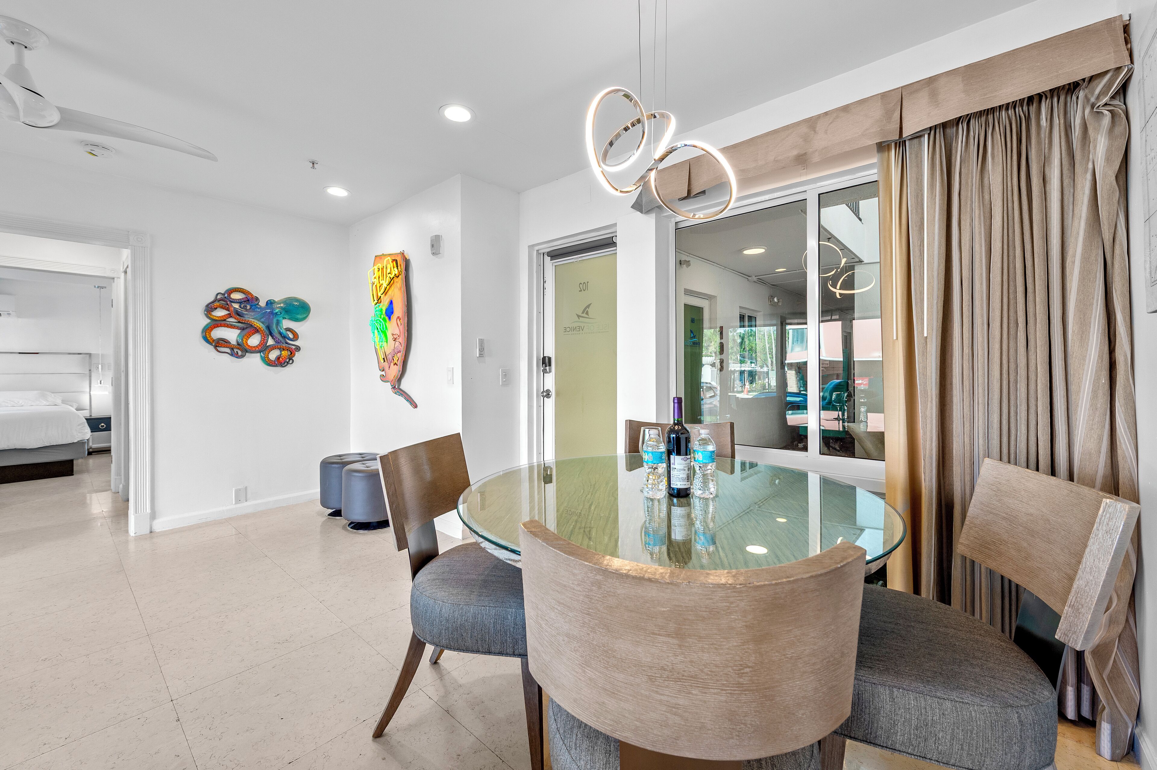 A modern dining area with a glass table, grey upholstered chairs, and a view of the adjacent room.