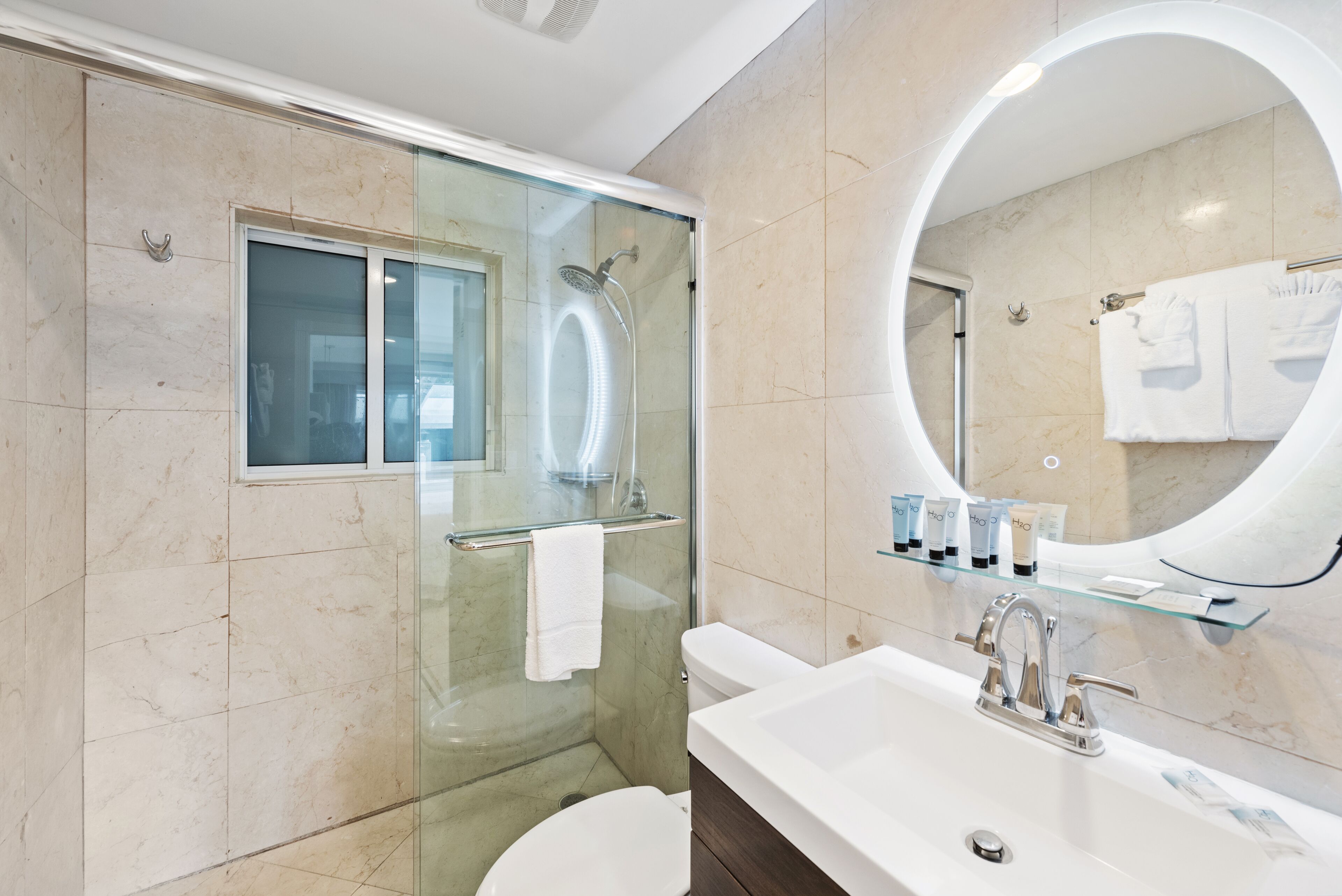 Een moderne badkamer met een douchecabine van glas, een wit wastafelmeubel met een glazen plank, en een grote spiegel.