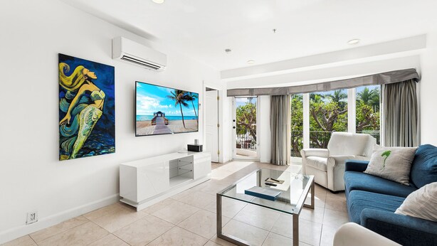 A modern living room with a TV, artwork, and a balcony with a view of the beach. - Isle of Venice (Fort Lauderdale)