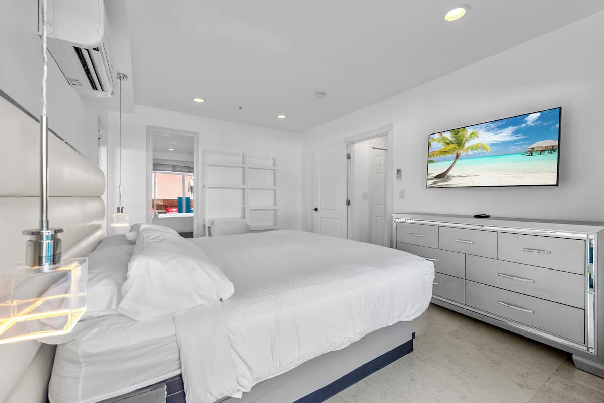 Quarto moderno com cama grande, televisão na parede e vista para a praia.