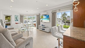 A modern living room with a flat-screen TV, comfortable seating, a glass coffee table, and a view of the outdoors. - Isle of Venice (Fort Lauderdale)