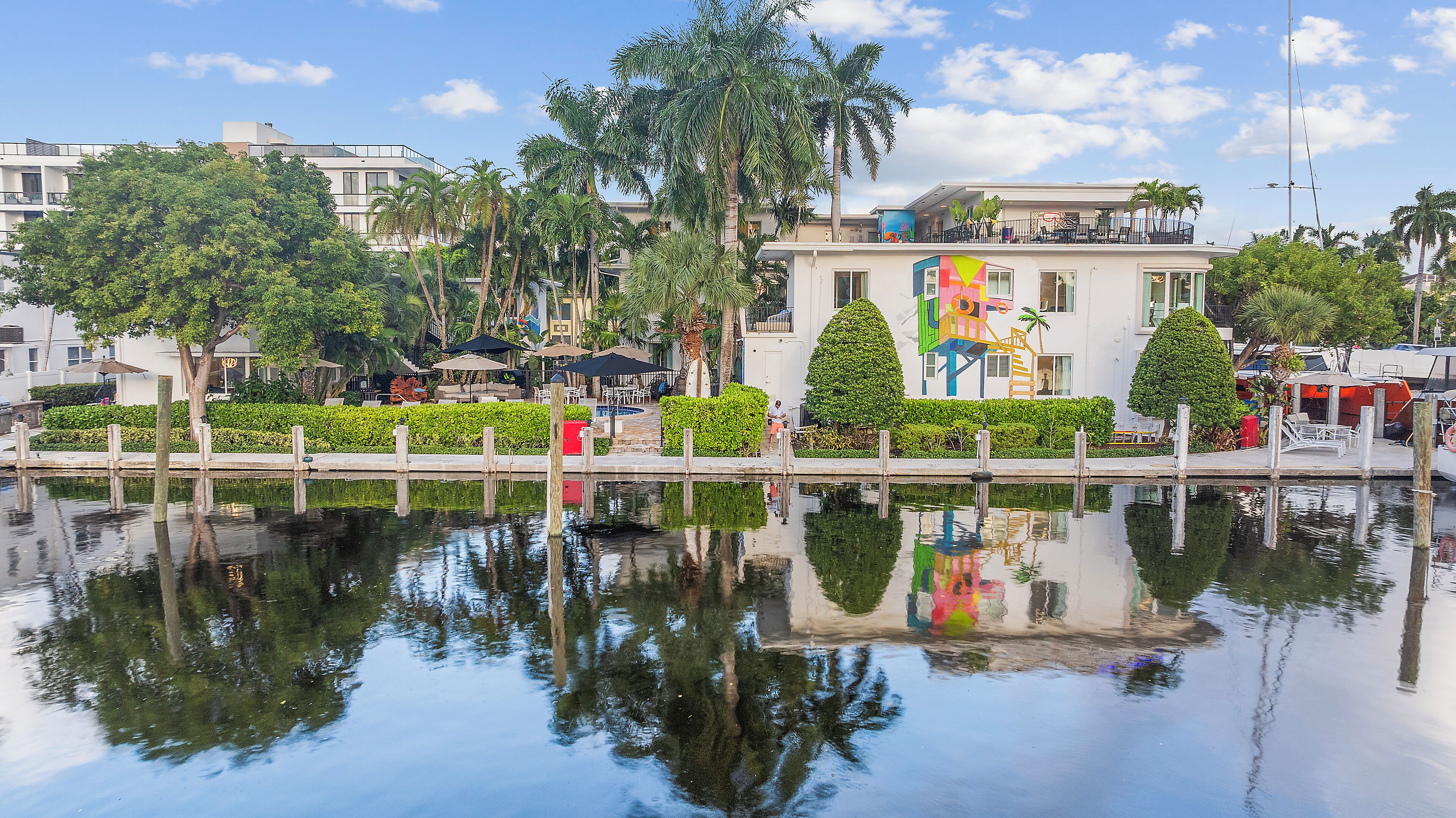 A waterfront hotel with a reflection in the water, a pool, and a colorful building with a unique design.