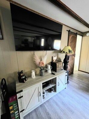 A living room with a mounted flat-screen TV, a wooden console table with decorative items, and a sliding barn door. - Charlie's Woodside Getaway-4 miles from the Dells! (Lyndon Station)