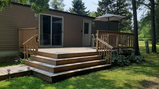 A wooden deck with steps leading to a sliding glass door, surrounded by a grassy yard and trees. - Charlie's Woodside Getaway-4 miles from the Dells! (Lyndon Station)