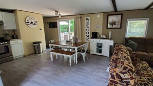 A cozy living area with a patterned sofa, a wooden dining table with chairs, a coffee station, and a kitchen area with cabinets and appliances. - Charlie's Woodside Getaway-4 miles from the Dells! (Lyndon Station)