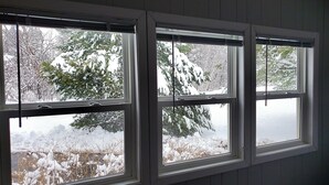 A room with three windows, each with a view of snow-covered trees and a frozen body of water. - Charlie's Woodside Getaway-4 miles from the Dells! (Lyndon Station)