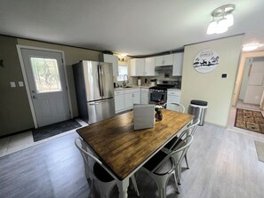 A modern kitchen with stainless steel appliances, a wooden dining table, and white cabinetry. - Charlie's Woodside Getaway-4 miles from the Dells! (Lyndon Station)