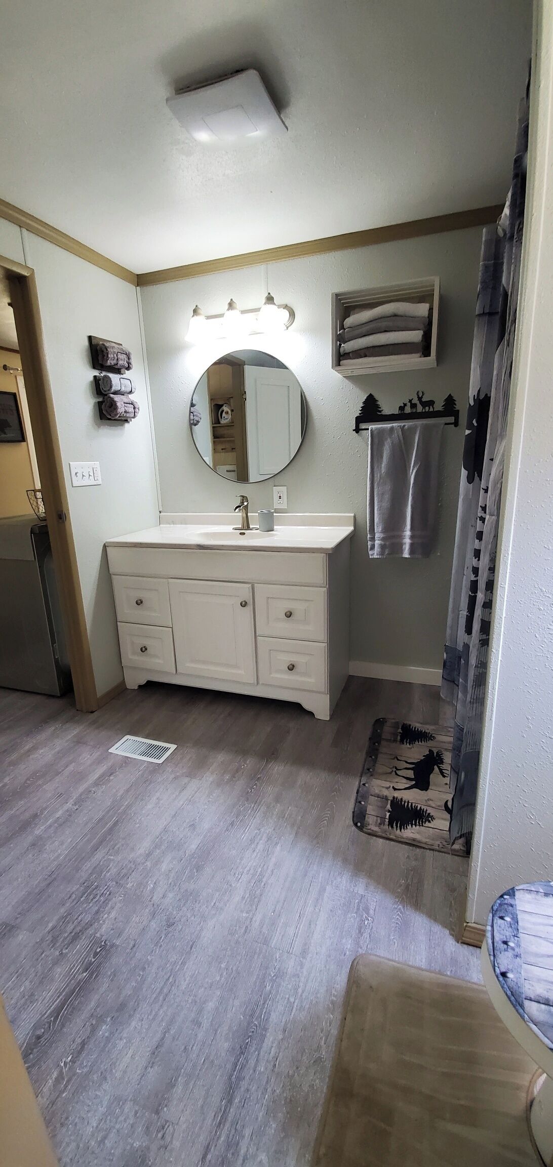 Une salle de bain avec un meuble-lavabo blanc, un miroir rond et un porte-serviettes.
