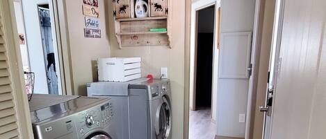 Een wasruimte met een wasmachine, droger en een plank met decoratieve objecten.