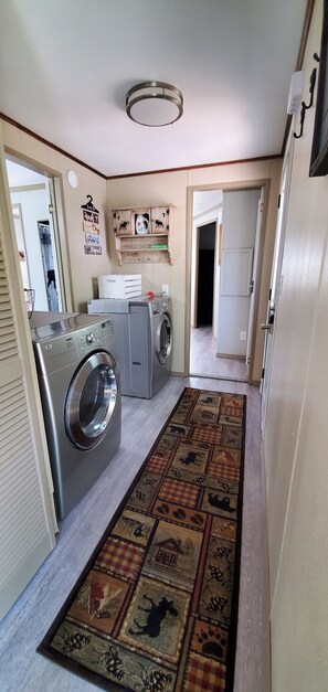 Un área de lavandería con lavadora, secadora y una estantería con objetos decorativos.