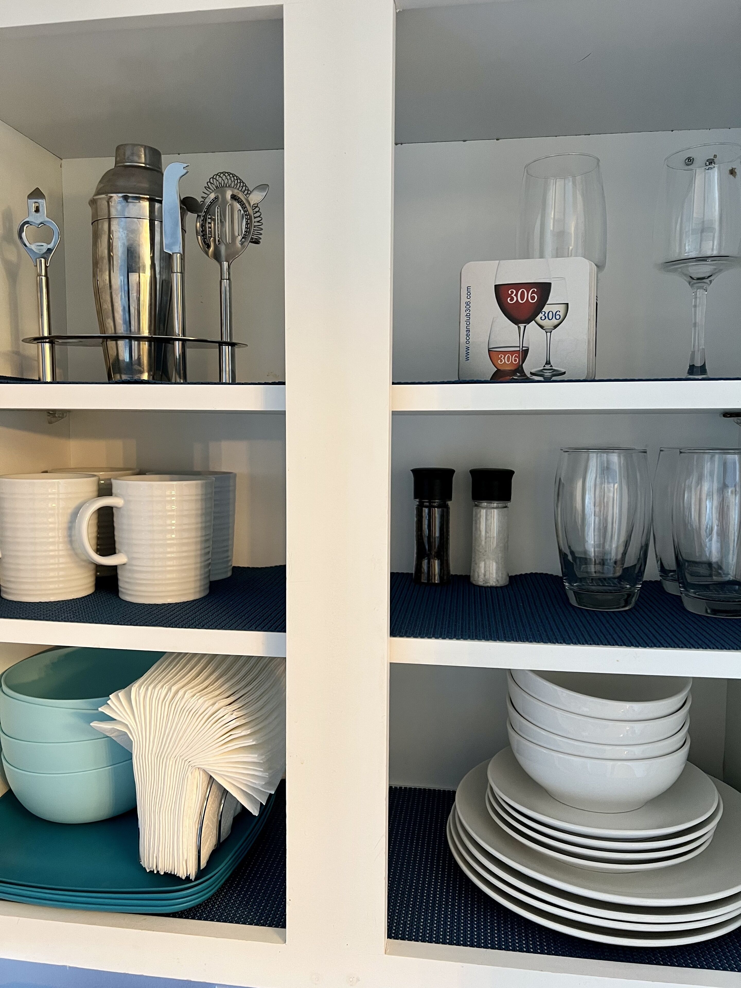 Une cuisine dotée de meubles blancs, d’appareils électroménagers en acier inoxydable et de divers ustensiles de cuisine, notamment des tasses, des assiettes et de la verrerie.