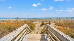 A wooden boardwalk leading to a beach with a clear sky and distant ocean view.