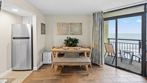 A compact living space with a kitchenette, a dining area with a bench, and a balcony with a view of the ocean.