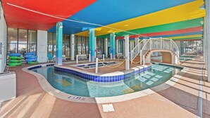 An indoor swimming pool with a colorful ceiling, a water slide, and a pool area with a tiled floor.