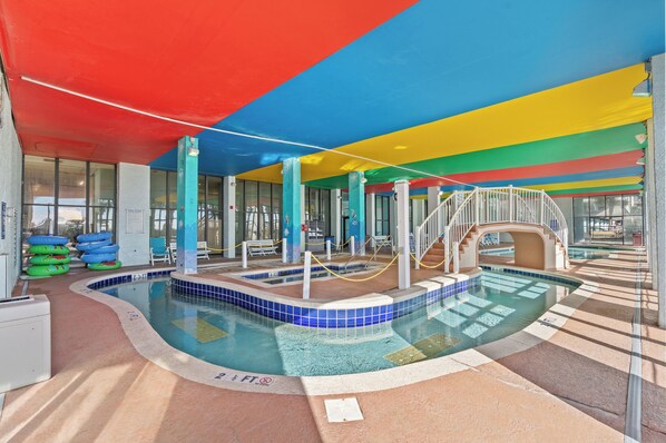 An indoor swimming pool with a colorful ceiling, a water slide, and a pool area with a tiled floor.
