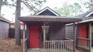 A small, single-story building with a red door and a porch. - 1 rm cabin, shared bth house, at Kick Back Ranch. (Ramer)