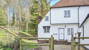 Une petite maison blanche avec un toit en tuiles, un portail en bois et un chemin de gravier menant à l’entrée.