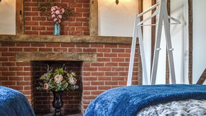 Une pièce avec une cheminée en briques, une échelle blanche et une couvre-lit bleue.