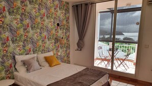 A bedroom with a bed, a small table, a balcony with chairs, and a view of the outside. - #Enjoy the charm of Studios 309 AbricotPays # (La Trinité)