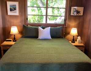 A bed with a green bedspread, two nightstands with lamps, and a window with a view of trees.