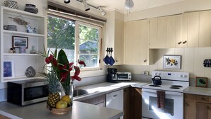 Een moderne keuken met witte kastjes, een magnetron, een broodrooster en een fornuis. Er is een raam met zonwering, een plafondventilator en een vaas met rode bloemen op het aanrecht.