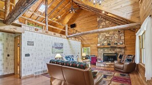 A log cabin interior with a fireplace, leather sofa, and a high ceiling with exposed beams.